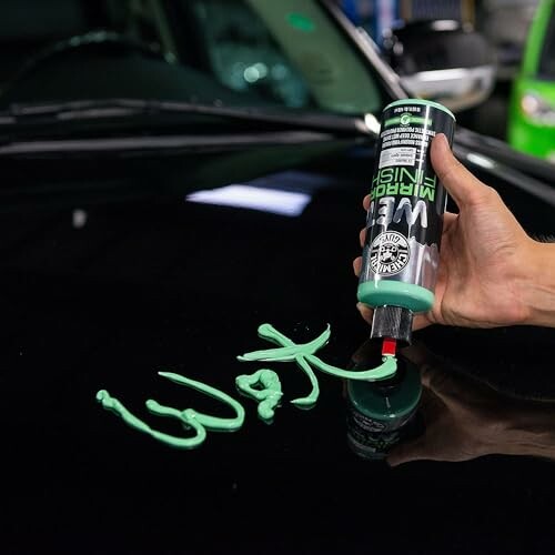 Hand applying green car wax on a vehicle surface.